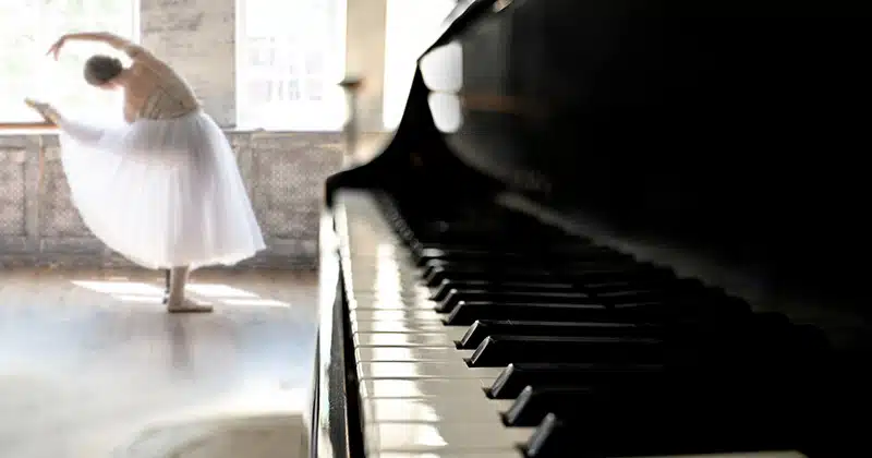 Ballerina stretches at bar with piano in forefront