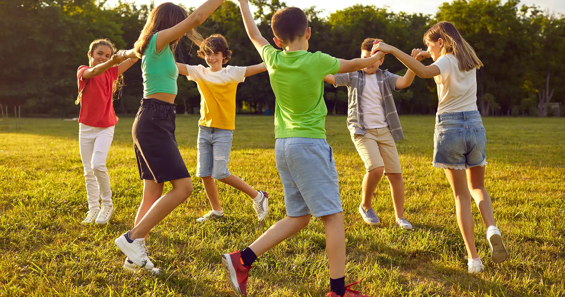 Group of kids dances in a circle outside while holding hands
