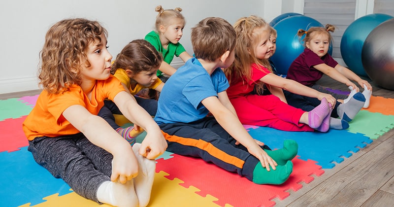 Group of preschoolers stretching on gym mats
