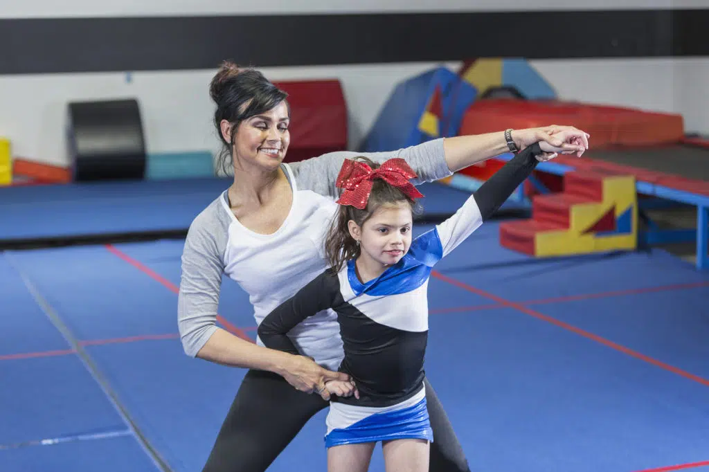 a coach teaching a young cheerleader