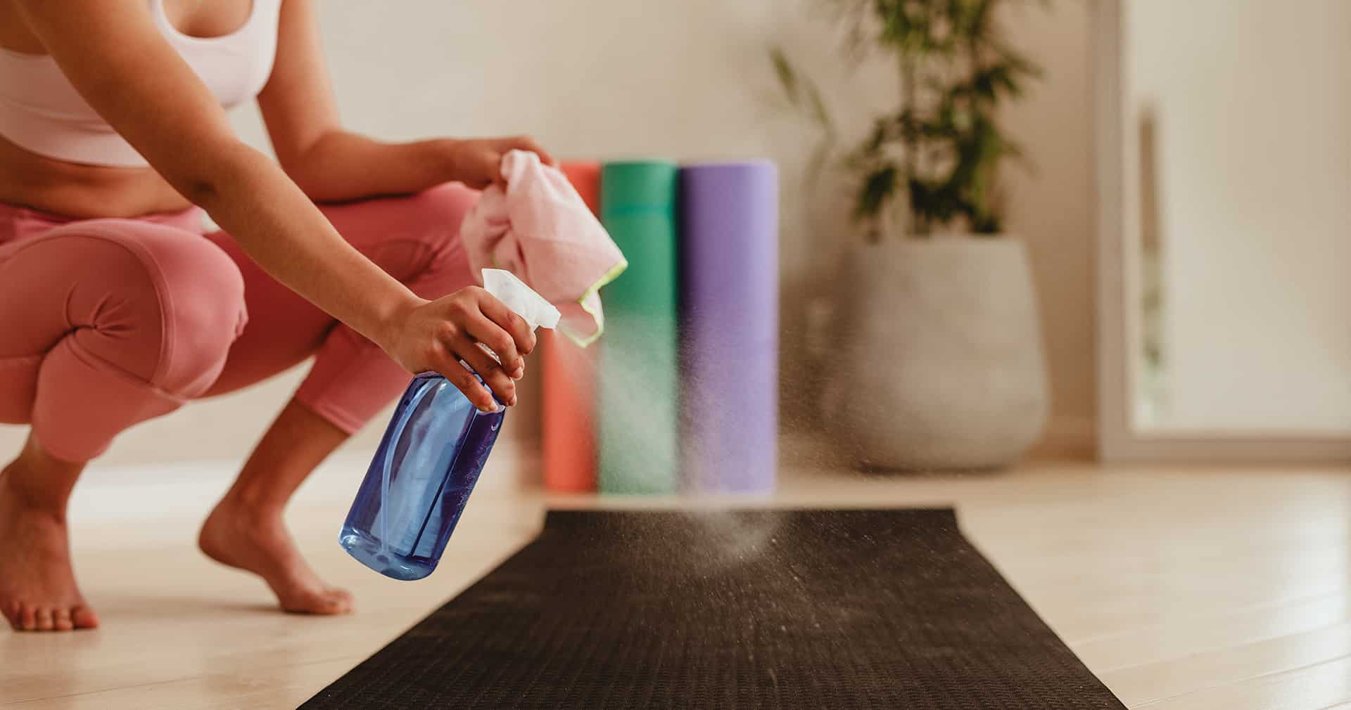 Person cleaning exercise mat with disinfectant spray in gym