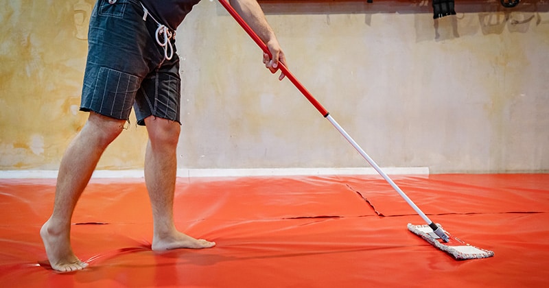 Person cleaning large mat with mop