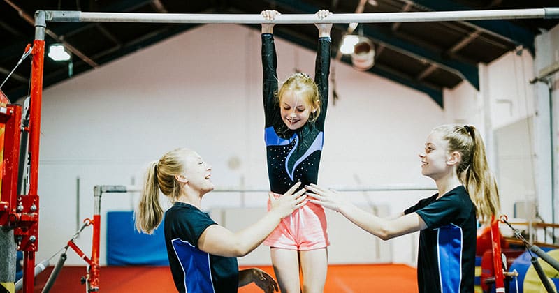 Two gymnastics teachers helping girl on high bar