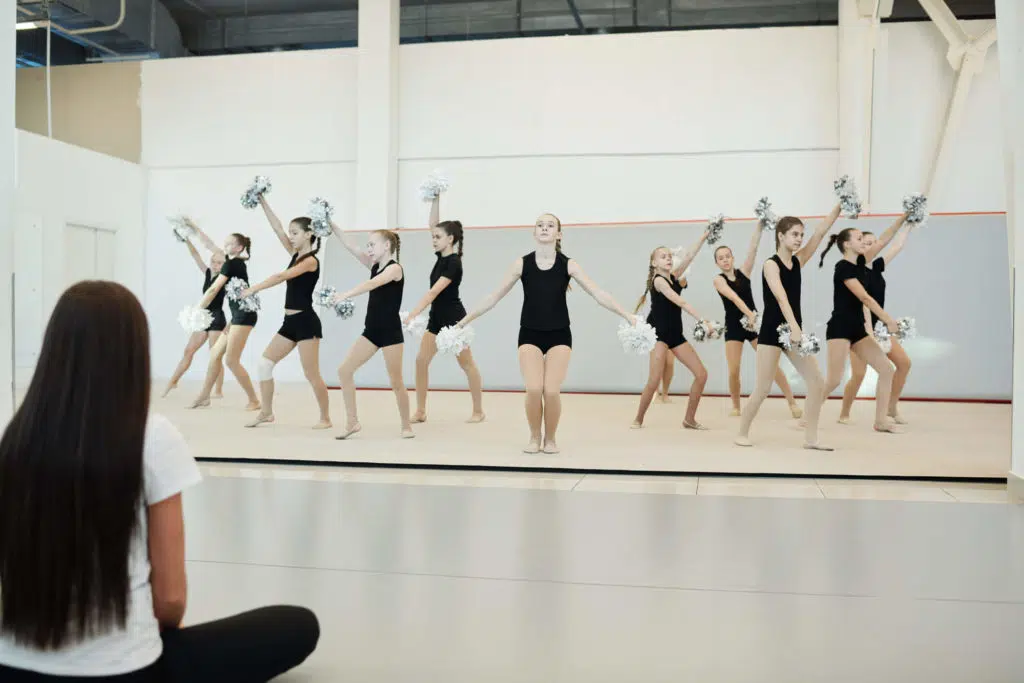 a cheerleading class on a mat demonstrating a routine to a teacher