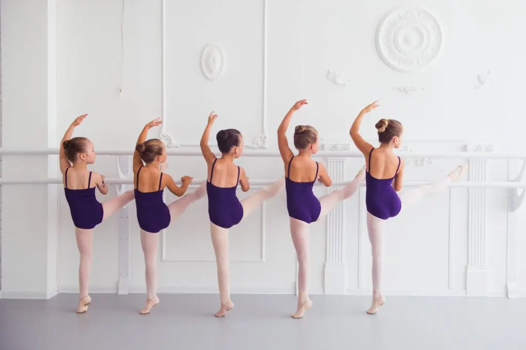 six girls at a ballet barre in a white dance studio