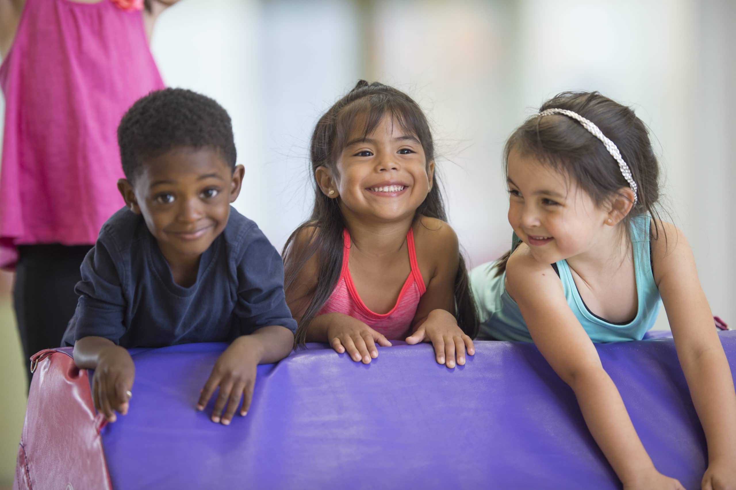 A multi-ethnic group of cute little kids are rolling on a mat together in gymnastics class.