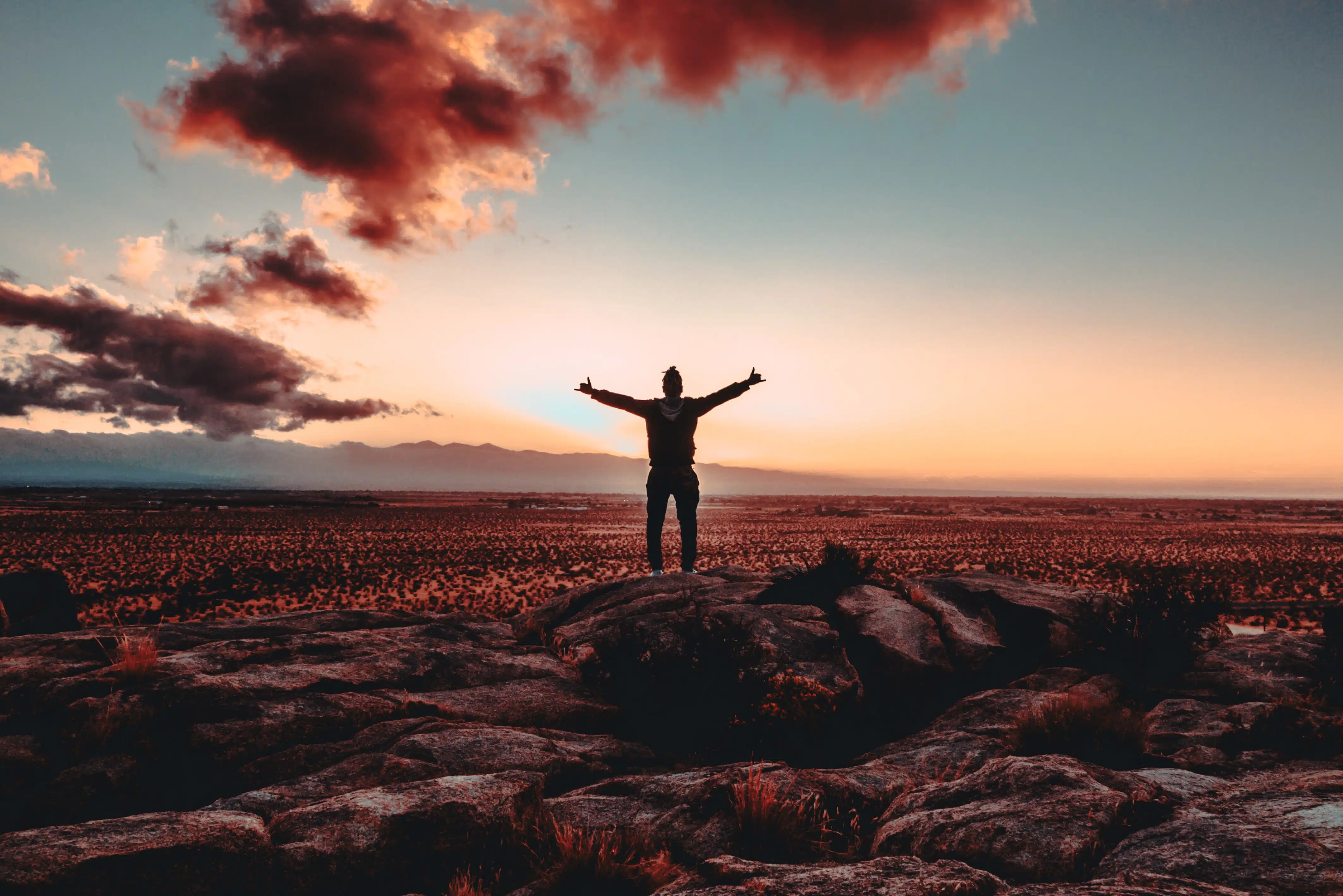 person standing on top of hill at sunrise with arms wide open