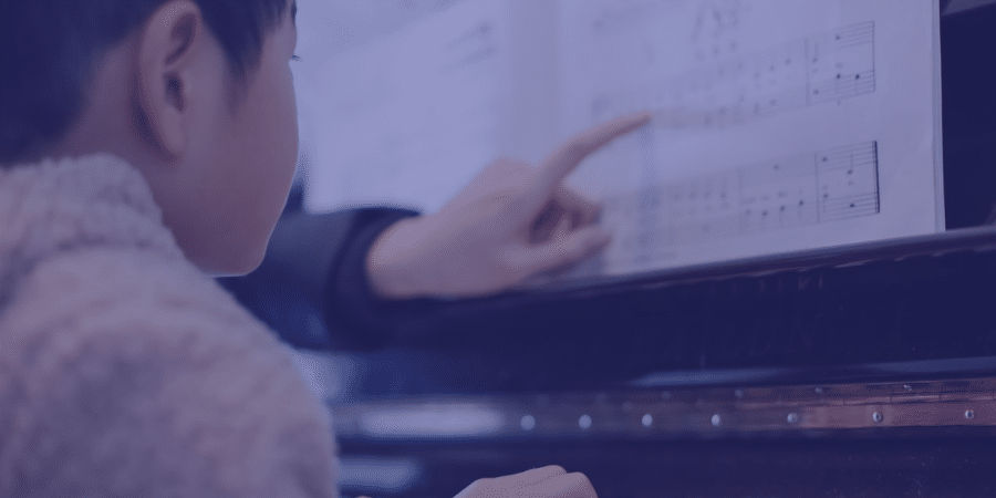 a teacher pointing to piano sheet music while a student sits there and learns