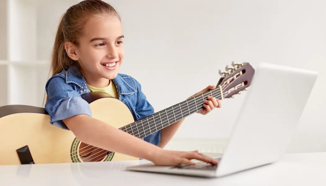 Cheerful girl with guitar using laptop